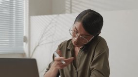 Close up of Asian businessperson talking on the phone and taking notes in notebook on desk with laptop computer in modern office. 4k 