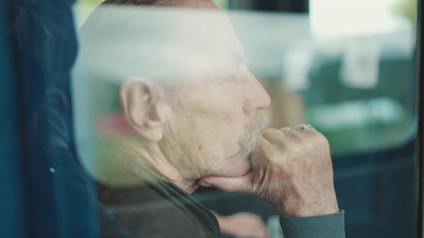 Closeup portrait of pensive elderly man looking out window while traveling in train coupe, view through glass