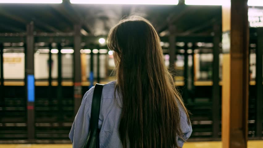 Young girl in the New York subway. Brunette woman standing on railway station, waiting for train. Girl in underground at evening looks on fast trams. Metropolis, freedom and active lifestyle concept. Royalty-Free Stock Footage #1108362455