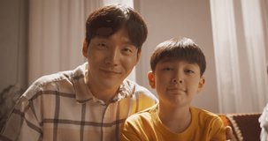 Portrait of a Happy Korean Father and Son in the Living Room at Home, Smiling and Waving at the Camera. Screen Replacement for Online Video Call With Friends. Family Using Technology to Stay Connected