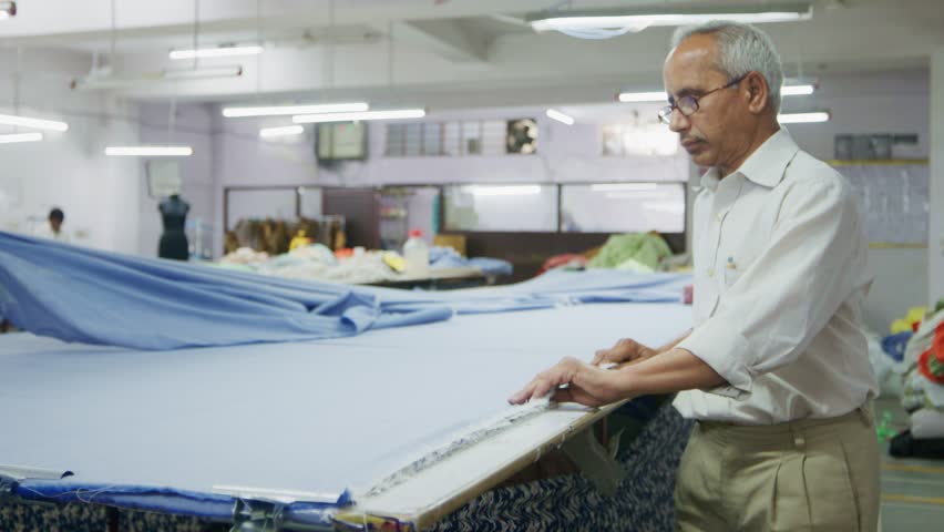 A skilled Indian man or male employee or artisan working with a large piece of cotton cloth or fabric in an indoor textile workshop or small-scale garment factory or industry Royalty-Free Stock Footage #1108363227