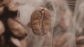 Macro slow motion video of a rotating coffee bean with an out of focus background of roasting coffee beans, the coffee grain is enveloped in smoke from the roasting.