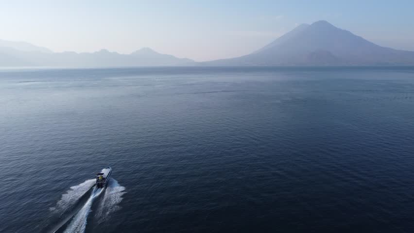 Aerial follows tourism tour boat on Lake Atitlan, GTM volcano mountain Royalty-Free Stock Footage #1108369387