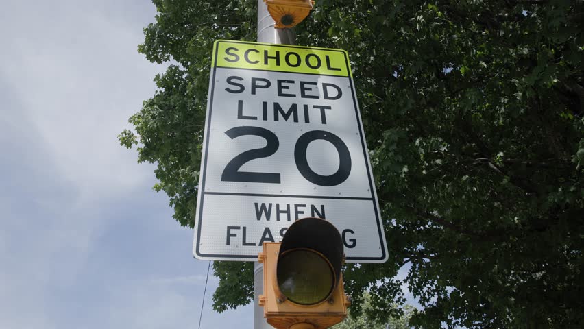 Handheld slow motion view of a school 20 miles per hour when flashing mph speed limit sign near educational building in suburb Royalty-Free Stock Footage #1108372613