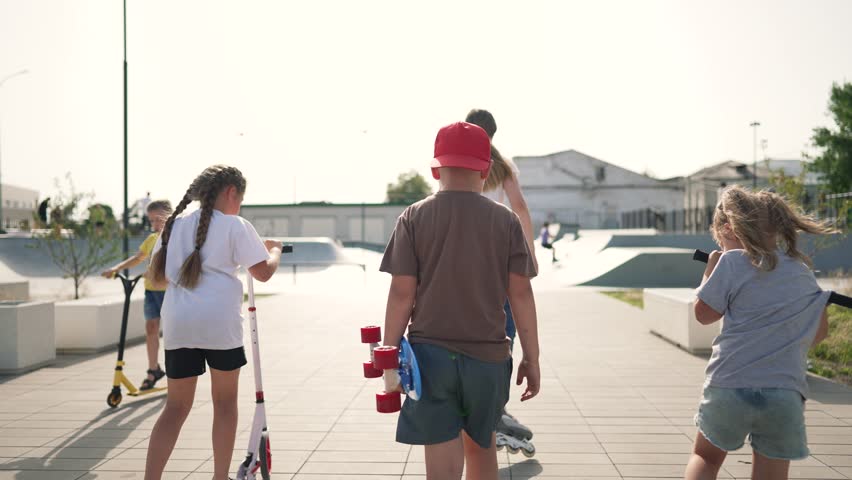 Children actively spend day in skatepark. group of friends are engaged scooter park roller skates, skateboard. Friends gathered in park. Children have fun outdoors on roller skates, skateboard,