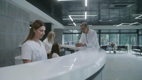 Adult woman comes to reception desk in clinic lobby area and makes appointment with doctor. Female administrator talks with patient at information counter. Medical staff work in modern medical center. - Powered by Shutterstock - Get 15% off with code: PIKWIZARD15