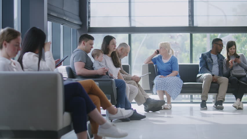 Diverse people sit on sofas in clinic lobby area, wait for doctors appointment. Doctor comes to family with child, talks about medical test results. Waiting room in modern medical center. Healthcare. Royalty-Free Stock Footage #1108377945