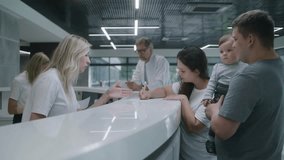 Family with kid stand near reception desk in clinic lobby area. Woman fills out documents, makes appointment with doctor, talks with female administrator. Medical staff work in modern medical center. - Powered by Shutterstock - Get 15% off with code: PIKWIZARD15