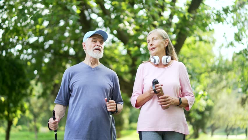 Happy active senior couple walking after workout in urban city park. Mature gray haired retired fitness man and woman spend leisure time together, have fun talking, enjoying a walk outside in nature Royalty-Free Stock Footage #1108383659