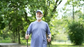 Senior active gray haired male with trekking poles walks in urban city park. Mature old fitness man practicing Nordic walking in nature in morning. Elderly pensioner is engaged in a scandinavian walk - Powered by Shutterstock - Get 15% off with code: PIKWIZARD15