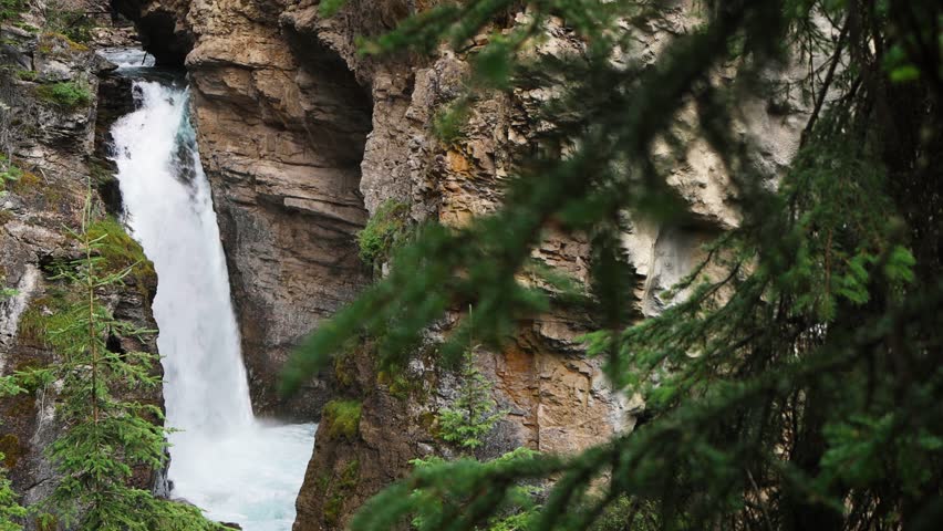 Turquoise water flowing through Johnstons Canyon, Banff National Park, Alberta, Canada. Waterfalls surrounded by green pine forests and mountain slopes.
