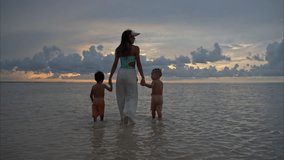 Young fit latin woman holding hands with two children walking in the shallow waters at a beach in Cancun Mexico at sunset