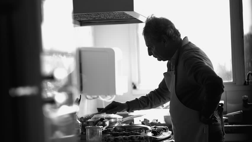 Monochrome scene of Elderly Chef Stirring Meal on Kitchen Stove, candid Older Man Focusing on Food Prep by Sink in black and white