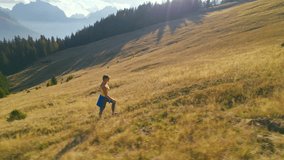 AERIAL: Fit lady walks up the autumn meadow with amazing views of high mountains. She is hiking with light feet and is enjoying magnificent alpine scenery that surrounds her. Nice sunny day in fall.