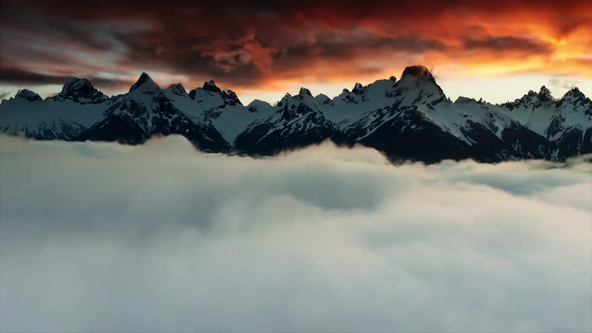 Flying through clouds to snow capped mountains at sunset