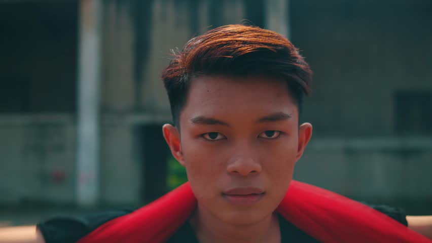 An intimate close-up portrait of a young Asian male dancer with styled, colored hair. He looks directly and intently into the camera with a calm, serious expression. 