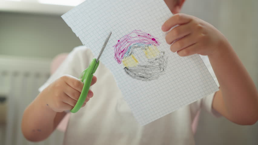 Cute little boy cuts out color drawing of checkered paper in art classroom closeup. Toddler child learns to use scissors at kindergarten lesson Royalty-Free Stock Footage #1108390015