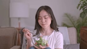 Lifestyle in living room concept, Young vegetarian Asian woman eating vegetable salad, healthy eating concept. - Powered by Shutterstock - Get 15% off with code: PIKWIZARD15
