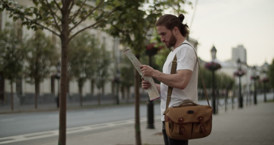 Male tourist checking map while standing on city street
