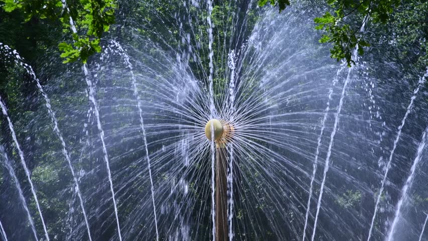 Close-up view of working dandelion shaped fountain jet nozzles with splashing water on city square in a sunny summer day. Real time handheld video. Soft focus. Urban decoration theme. | Shutterstock HD Video #1108393763