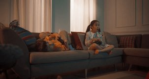 Cute Little Siblings Playing Video Game On Gaming Station On The Sofa In Cozy Living Room. Korean Brother And Sister Enjoying Games Together In The Evening. Children Having Fun At Home After School.