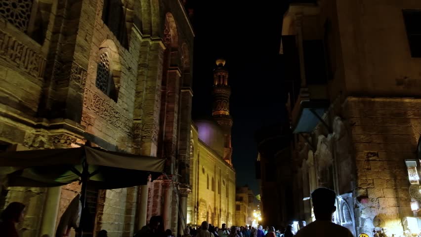 People walking around streets of Khan El Khalili bazaar in Cairo, Egypt. Night Cairo street. Minaret of Complex of Sultan al-Mansur Qalawun at background Royalty-Free Stock Footage #1108394899