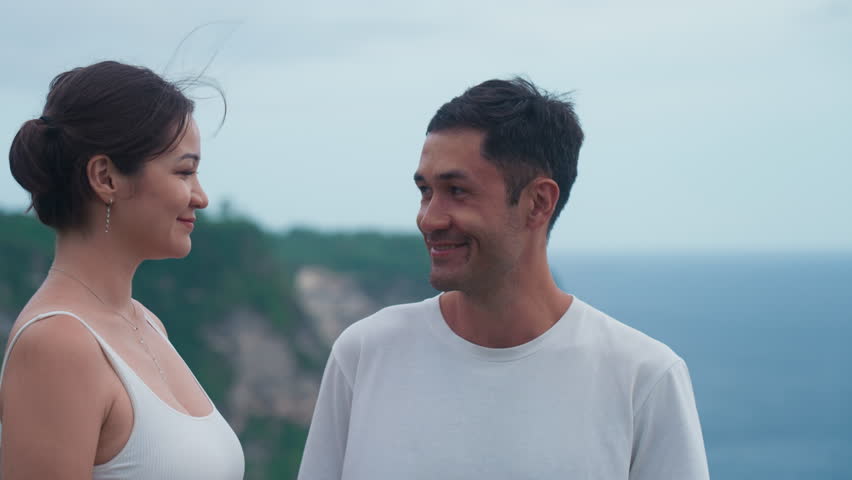 Asian man and woman look at each other and talk sweetly in embarrassment. Enthusiastic emotional happy Korean couple. Moments of traveling on wild seashore during summer holidays. Vacation on island Royalty-Free Stock Footage #1108395623