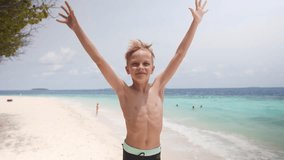 Happy caucasian child boy jumping and greeting hand wave to say hi on the beach during summer vacation, video portrait. High quality 4k footage