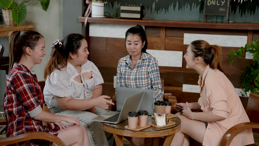 Group of Asian female coworkers chatting at a table in cafe using a laptop computer shop Online shopping in coffee shop during the day Order drinks and bakery items Come sit and eat at table together. Royalty-Free Stock Footage #1108403763