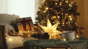 Merry Christmas! Hands in cozy sweater putting delicious gingerbread cookies on table against stylish gifts and christmas tree with lights in cozy room. Atmospheric christmas eve footage