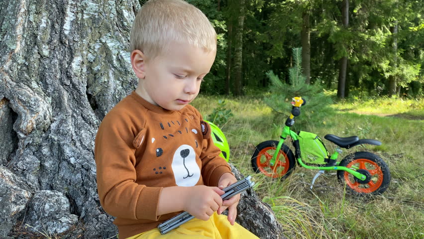 toddler child playing with multitool in summer forest, little boy with balance bike in park