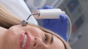  Close-up of a young woman's face during microcurrent therapy. Cosmetic procedures. Vertical video