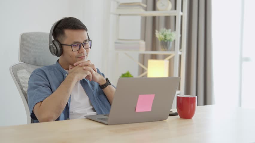Asian freelance business man wearing headphones making video call in home office, using laptop, talking, watching webinar or studying language, speaking, online training, explaining, e-learning. Royalty-Free Stock Footage #1108419003