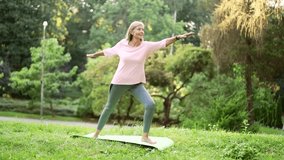 Senior active gray haired woman does gymnastics while standing on a mat in an urban city park. Mature old fitness female doing yoga outside. Elderly sportswoman performs muscle stretching exercises - Powered by Shutterstock - Get 15% off with code: PIKWIZARD15