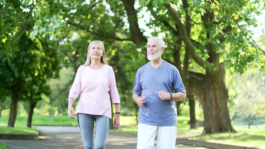 Senior gray haired man suffers from painful severe knee joint ache during a run in city park. Mature old wife supports her husband. Trauma injury while jogging outdoors. Leg muscle cramp calf sport Royalty-Free Stock Footage #1108422585