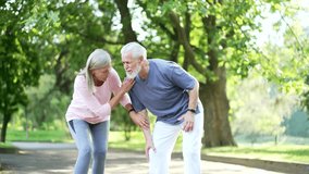 Senior gray haired man suffers from painful severe knee joint ache during a run in city park. Mature old wife supports her husband. Trauma injury while jogging outdoors. Leg muscle cramp calf sport - Powered by Shutterstock - Get 15% off with code: PIKWIZARD15
