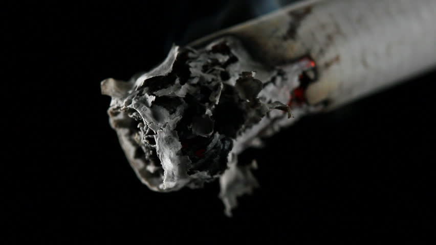 Closeup of a cigarette burning with smoke flowing up into the darkness