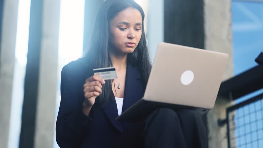 Confused businesswoman with credit card thoughtfully pondering on screen while has problem with online order payment error or blocked bank account doing shopping at internet on laptop at modern city Royalty-Free Stock Footage #1108425585