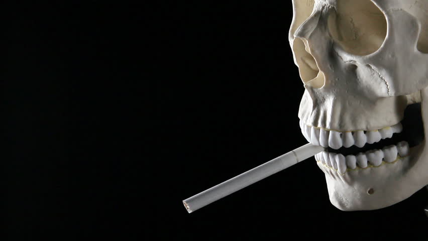 Closeup of a cigarette burning in a human skull's mouth with smoke flowing up