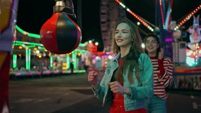Smiling girl hitting boxing machine at amusement park. Cheerful teenagers having fun celebrating high score in game. Happy friends enjoying funfair evening hang out together. Weekend leisure concept - Powered by Shutterstock - Get 15% off with code: PIKWIZARD15