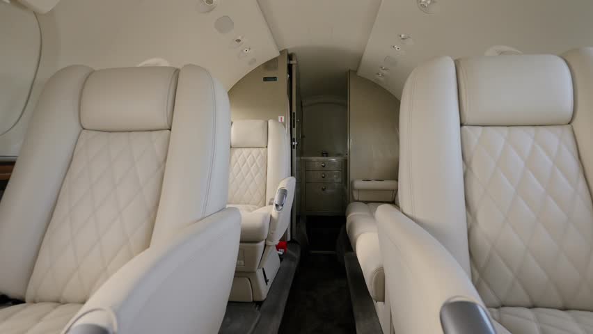 Cabin interior of private business aircraft arranged with several beige leather seats and couch. Bright exquisite salon of jet with portholes and ceiling lights Royalty-Free Stock Footage #1108429095