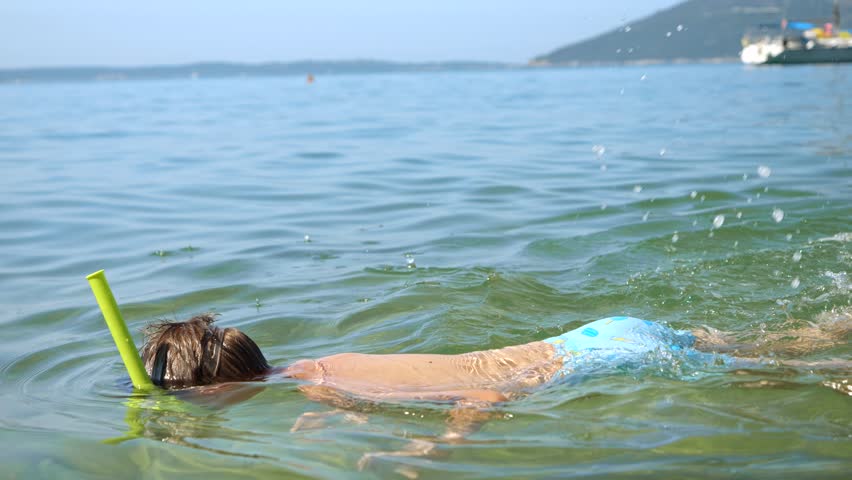 Slow motion of little boy wearing snorkeling mask diving underwater and watching fishes in sea