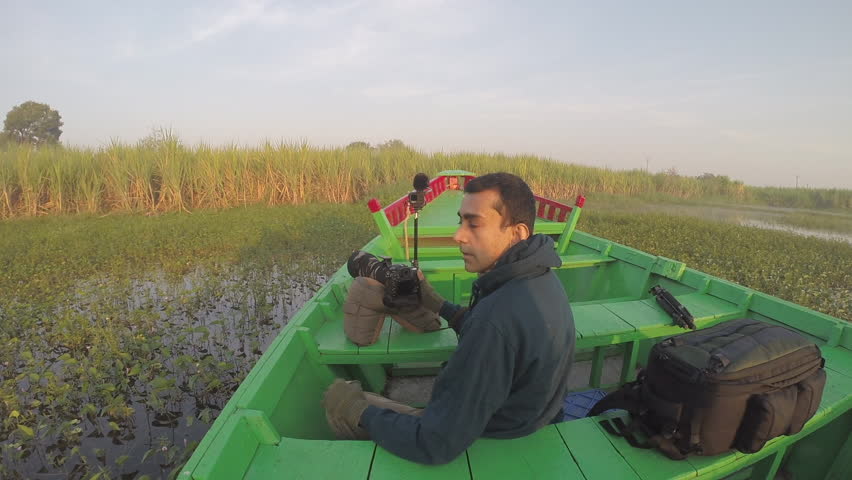An Indian wildlife photographer clicking photos of birds and animals from a boat in on a lake with a DSLR camera and telephoto lens