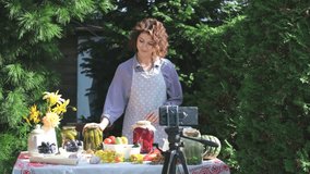 A woman shoots a video on a smartphone while preparing canned vegetables for the winter. On a warm autumn day, a housewife leads a video blog, teaches her subscribers the process of pickling and
