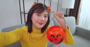 Young asian woman holding smartphone and talking with pumpkin toy in hand at living room. She preparing to join in halloween party.