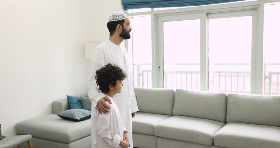 Loving Muslim father hugs his little son standing in living room looking out window, spend time together, feeling unconditional love, having good, friendly relations between kid and dad. Family ties Royalty-Free Stock Footage #1108437755