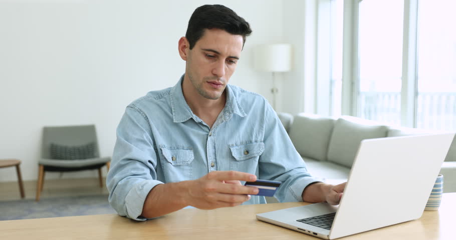 Millennial guy, satisfied shopper enters credit card data makes payment via on-line web store using laptop, pay bills, spending money on internet, getting cashback enjoy e-commerce e-shopping at home | Shutterstock HD Video #1108437773