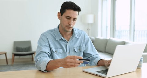 Millennial guy, satisfied shopper enters credit card data makes payment via on-line web store using laptop, pay bills, spending money on internet, getting cashback enjoy e-commerce e-shopping at home 스톡 비디오