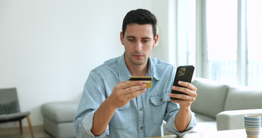 Angry young man having problem with on-line payment, holds mobile phone and card feels indignant due to insufficient funds to make purchase on internet, scam or fraud, online theft, e-payment failure Royalty-Free Stock Footage #1108437829
