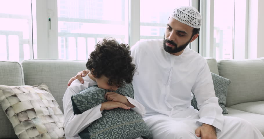 Worried Muslim father sit on sofa stroking shoulder, supporting, consoling offended little son, suffer from bullying in school, asking for forgiveness after quarrel, apologizing, showing love and care Royalty-Free Stock Footage #1108437857